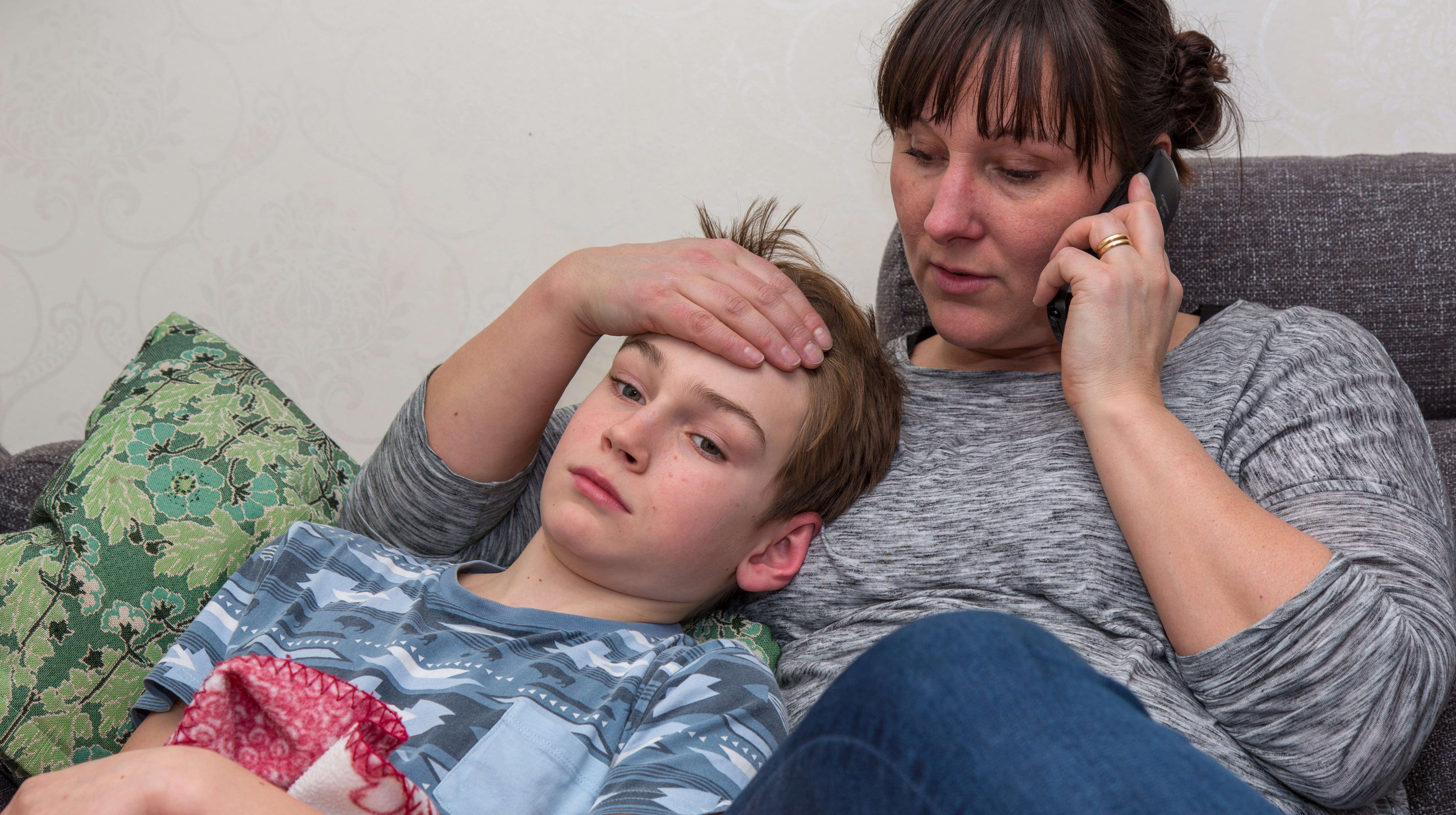 Kvinna som pratar i telefon och stryker sjuk pojke över pannan