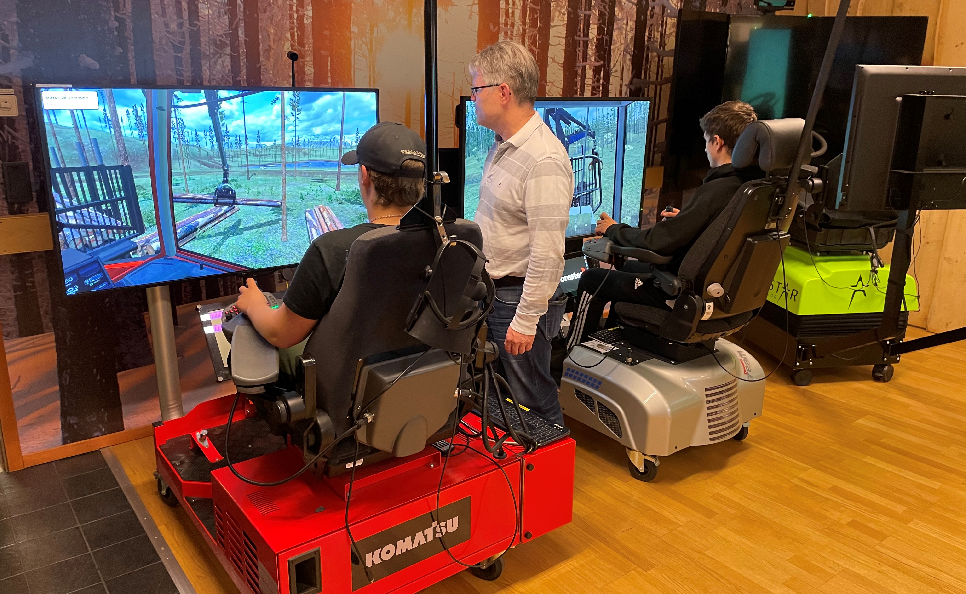 Två elever sitter i simulatorer med lärare som instruerar