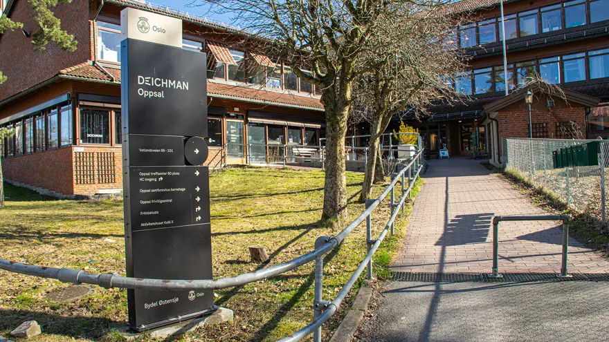 Exteriör av biblioteket och byggnaden det ligger i. En gångväg går upp till byggnaden som är i två våningar och byggd i rött tegel. Den sitter ihop med en annan trevåningsbyggnad i samma stil. Solen skiner och det är vår ute.