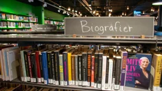 En låg bokhylla fylld med böcker. Ovanpå hyllan finns en skylt med texten "Biografier". Skylten är en svart tavla och texten skriven med vit krita.