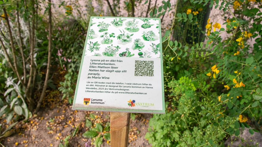 En liten skylt på en trästolpe. Den står i en blommande rabatt. På skylten finns bland annat en QR-kod och texten: "Lyssna på en dikt från Litteraturbanken".