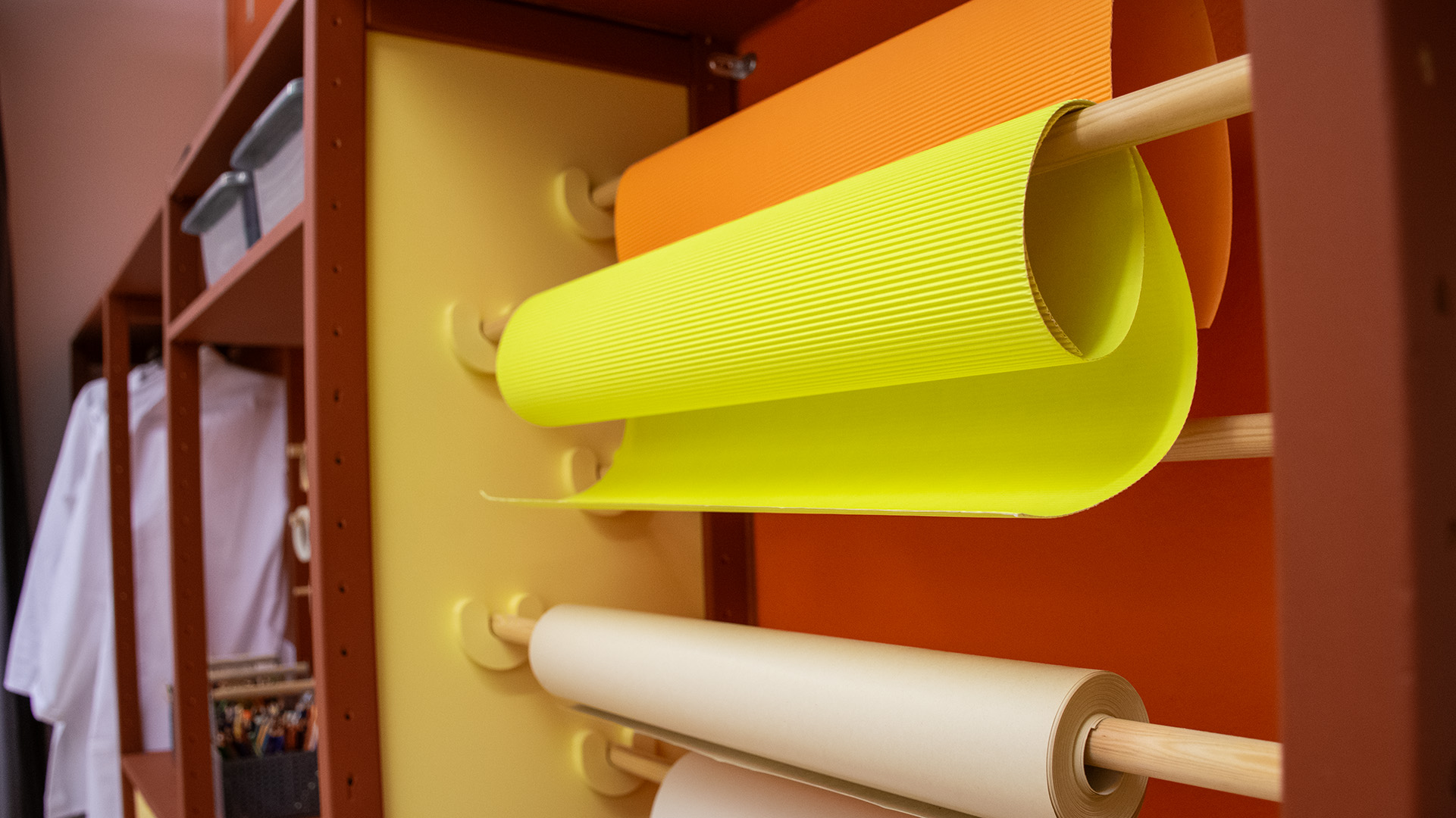 Rullar med färgglada papper hänger på rullar på väggen. Längre bort finns vita labbrockar på en stång. 