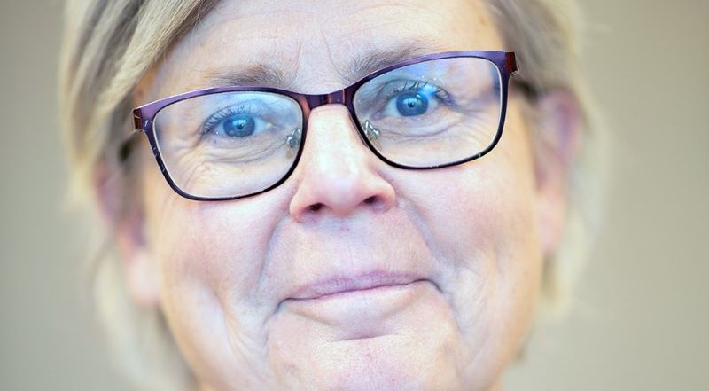 Kvinna, blont, kort hår. Glasögon med mörka bågar.