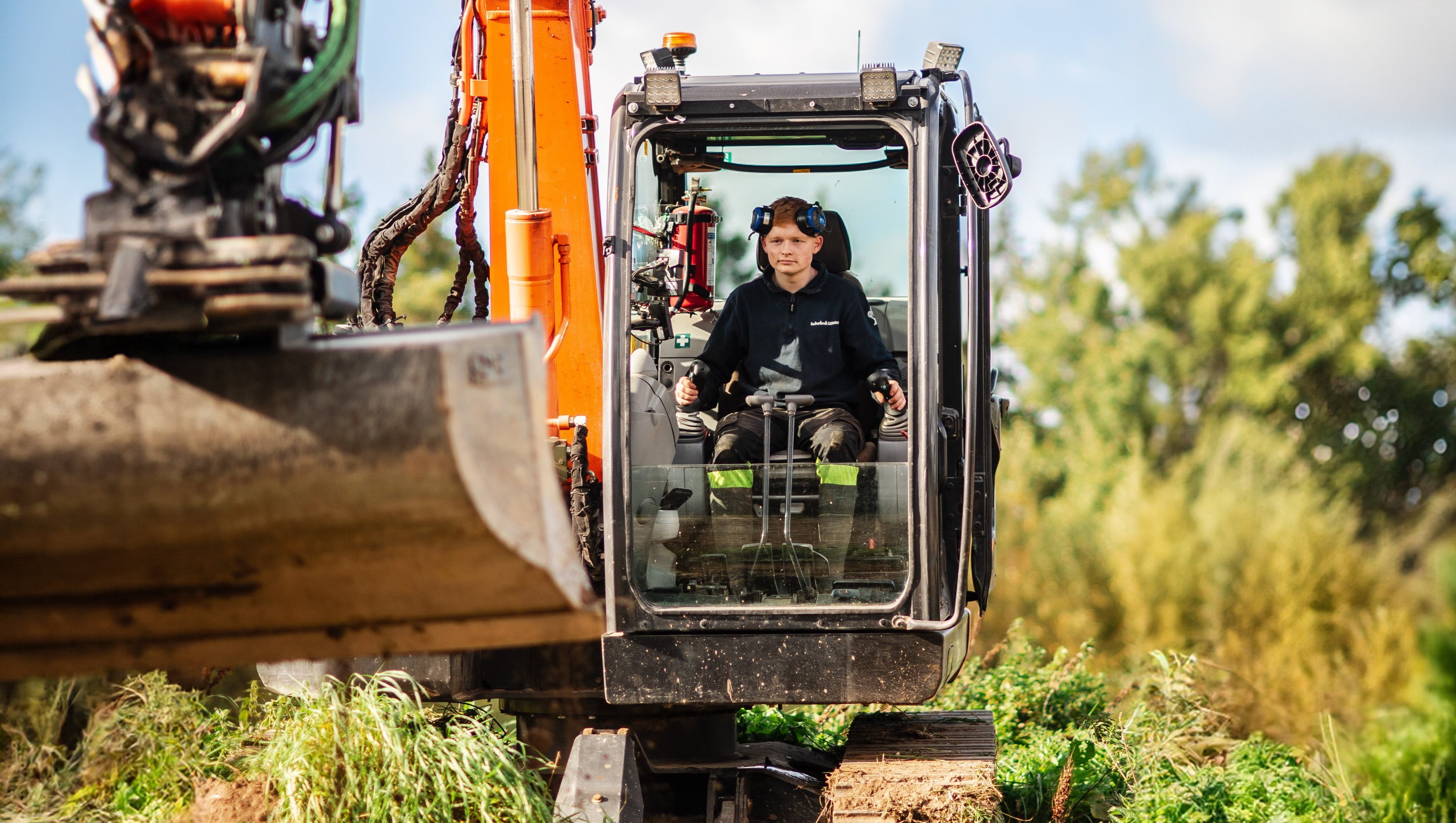 Elev sitter i grävmaskin med skopan i förgrunden