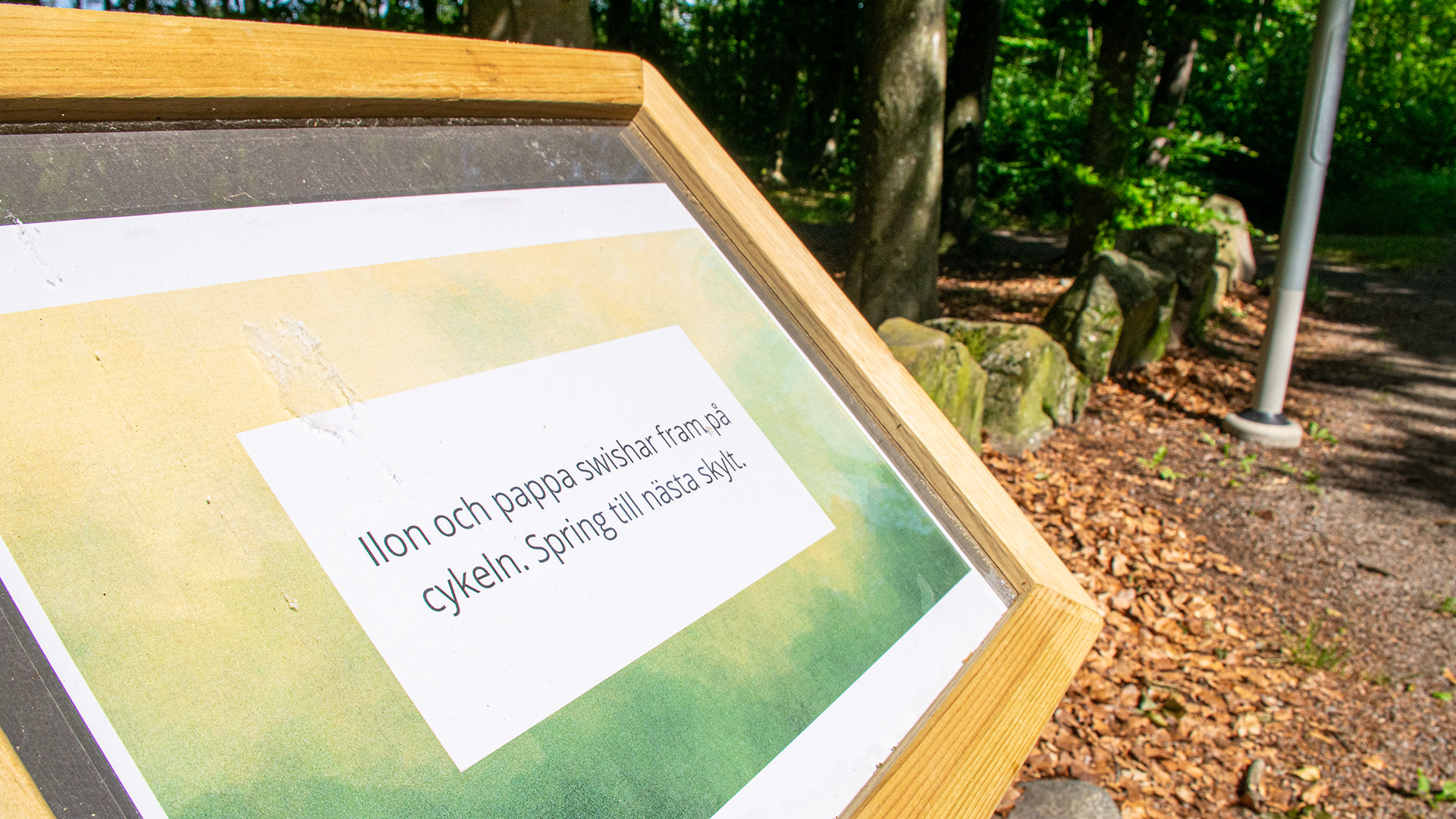 Närbild av en skylt med texten: "Ilon och pappa swishar fram på cykeln. Spring till nästa skylt". 