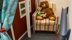 En fåtölj där en stor nalle och katten Findus sitter. Fåtöljen står i ett litet hörn, på ena sidan syns snickerboas röda vägg, på andra sidan två rör på väggen som man kan rulla bollar i.