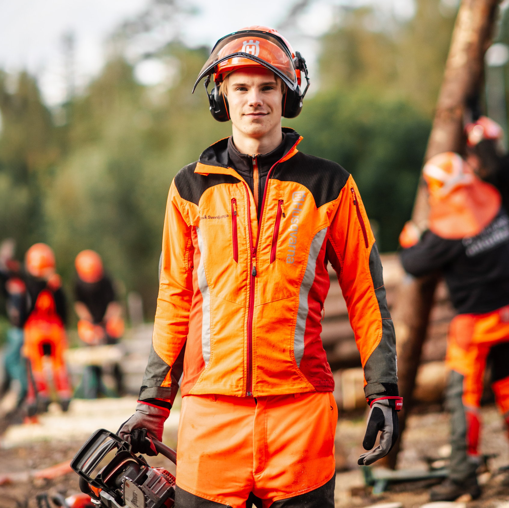 Elev med skyddshjälm och orange skyddskläder håller i motorsåg