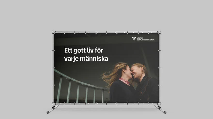 Stor vepa med bild på två leende kvinnor med ansiktena mot varandra. De ser förälskade ut. På bilden finns budskapet Ett gott liv för varje människa och VGR:s logotyp längst upp i högra hörnet