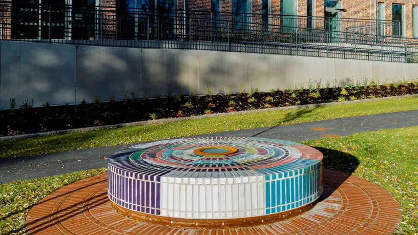 Rundel med färgade kakelplattor på en gräsmatta. I bakgrunden en röd tegelbyggnad.