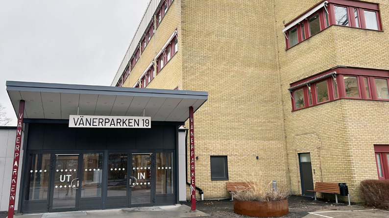 Entré med glaspartier brevid gul tegelbyggnad